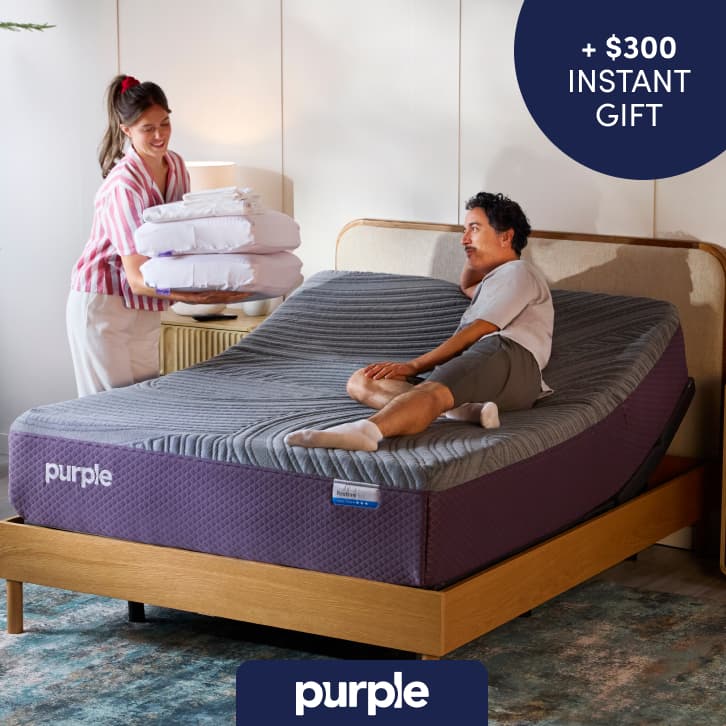 Adjustable Purple Restore Cool Touch mattress in a modern bedroom, shown with two people relaxing on the bed; promotion offering up to $500 off.