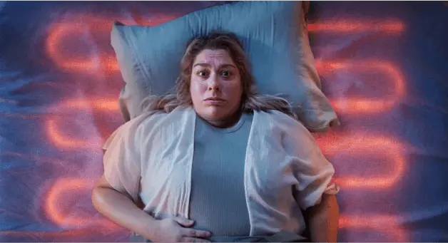 Person lying on a mattress with their head on a pillow, surrounded by red and blue lighting.