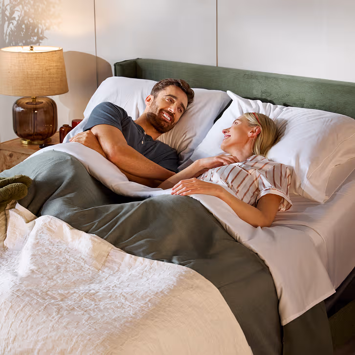 Two people relaxing on an adjustable mattress in a modern bedroom, highlighting a free adjustable base promotion on select mattresses.
