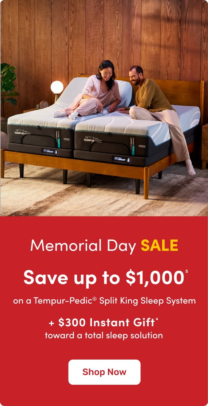 Tempur‑Pedic split king adjustable bed with two people reclining in a modern bedroom, Memorial Day sale promotion offering up to $1,000 savings and a $300 instant gift.